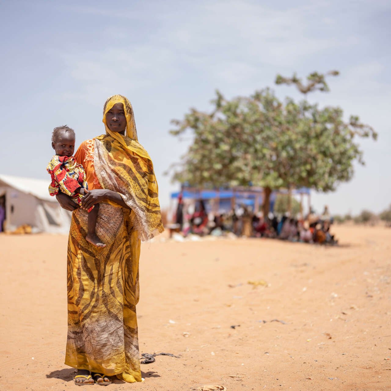 En kvinna på flykt står i ett torrt landskap i Chad och håller sitt barn i famnen.