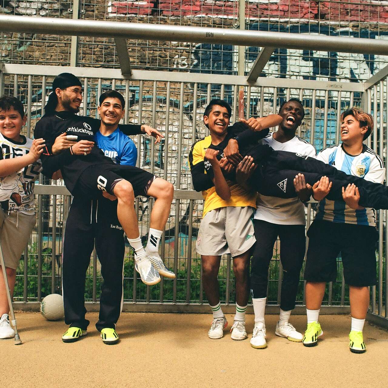 Eine Gruppe von Kindern posiert lachend in einem Fußballtor, wobei einige von ihnen andere Kinder auf den Armen tragen.