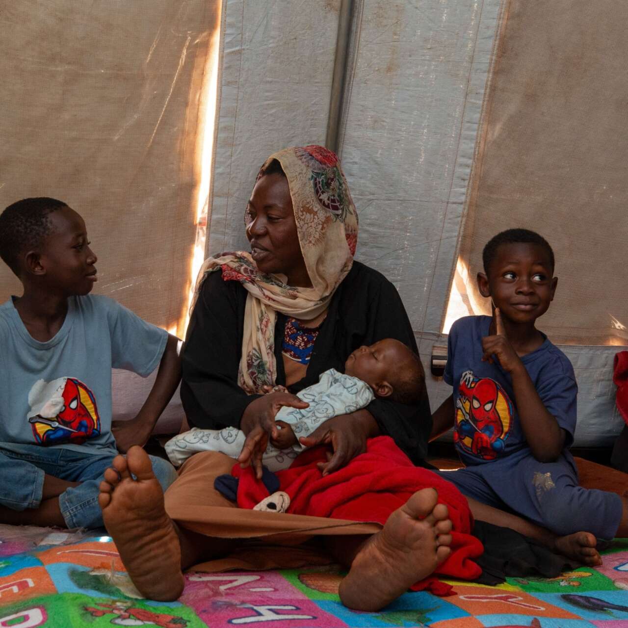 A family sits together on the floor of a makeshift shelter in a camp for displaced people.