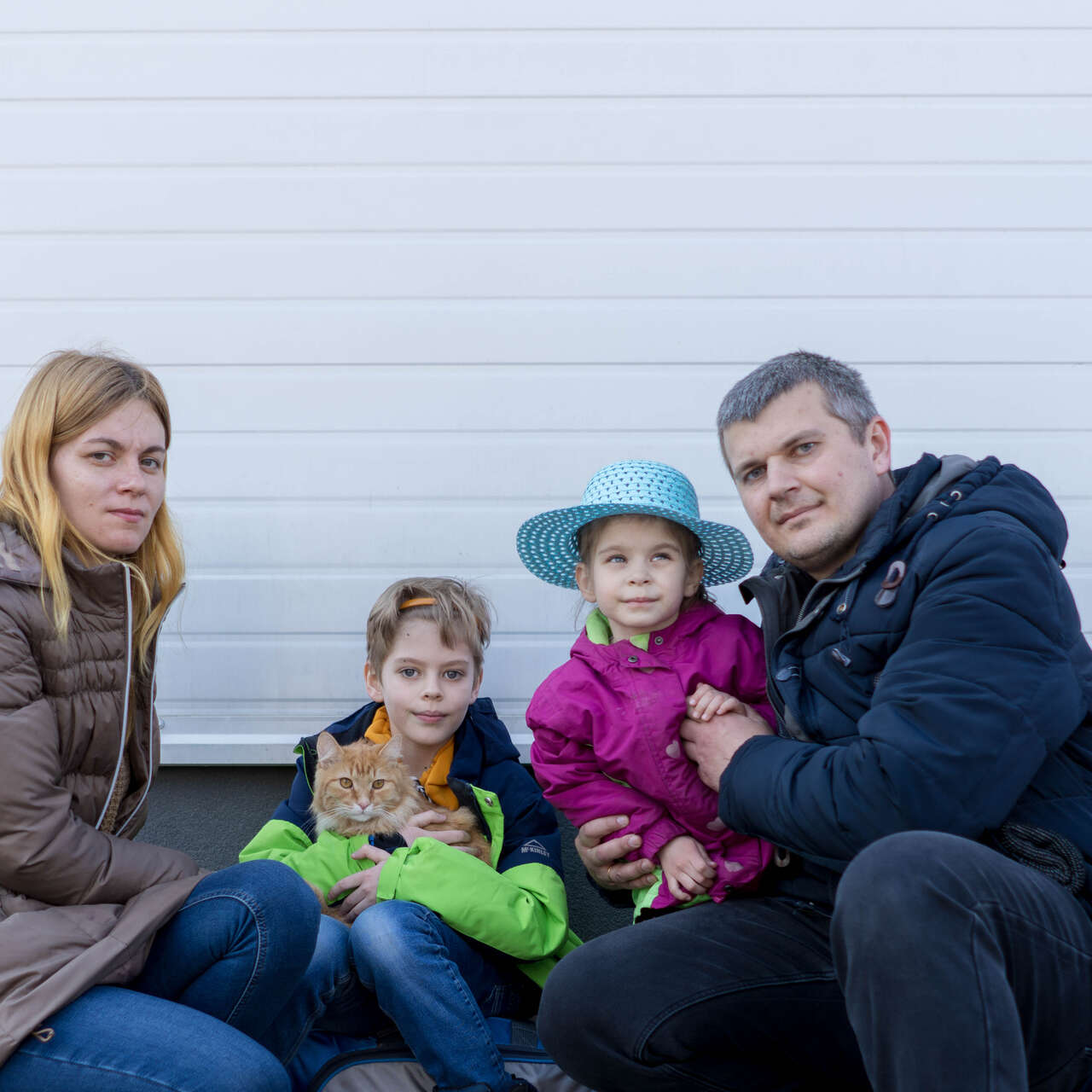 A Ukrainian family poses for a photo outside. A young son holds the family's cat.
