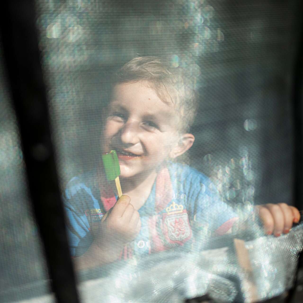 Ein lachendes Kind schaut durch ein Fenster und berührt die Scheibe mit den Händen.
