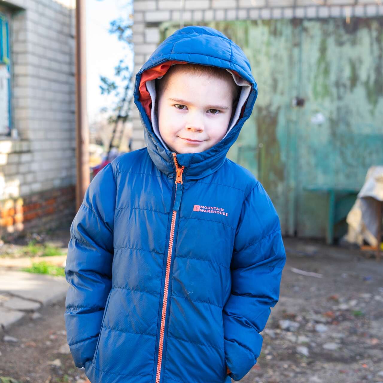 Ein kleiner Junge in einer blauen Jacke posiert für ein Foto und lächelt sanft in die Kamera.