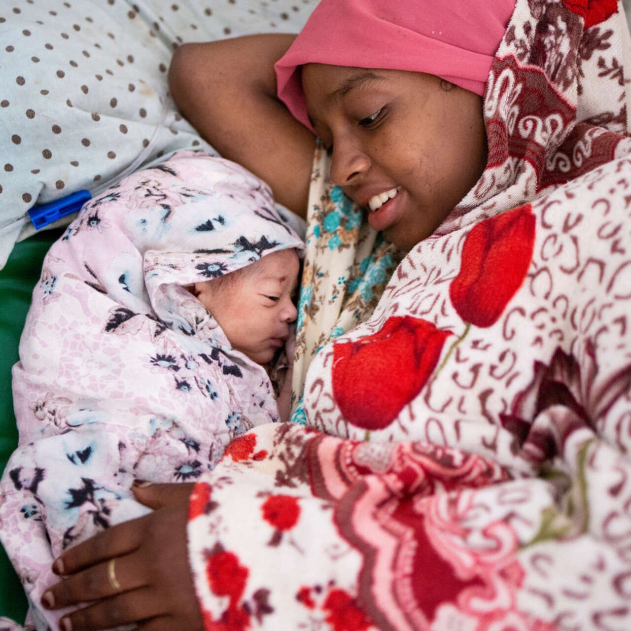 En kvinna i Etiopien ligger i en säng bredvid sin nyfödda bebis och ler mot honom.