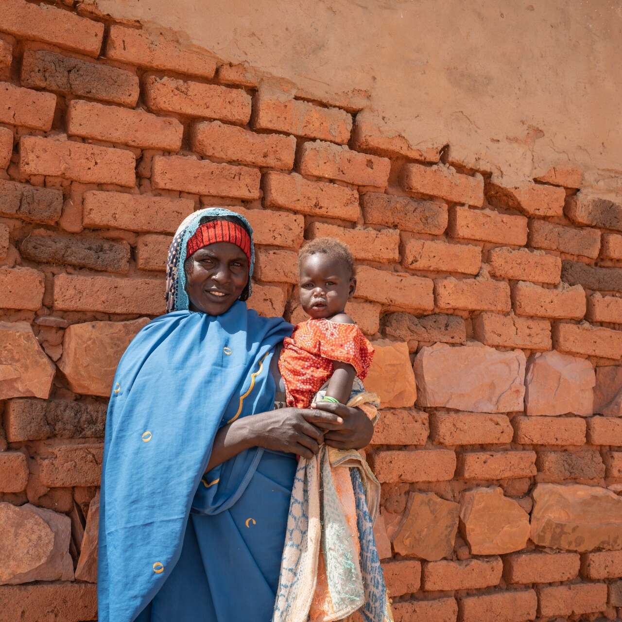 A mother holds her young daughter on the hip. They pose for a photo outside their home in Chad.