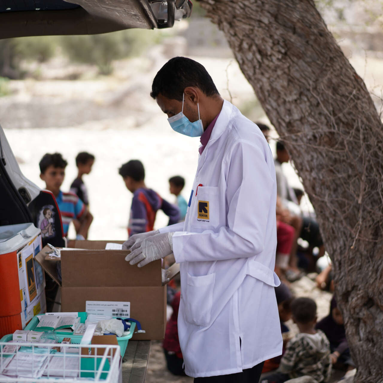 RESCUE:s personal i Jemen står vid bakluckan av en bil och tar fram mediciner medan barn leker i bakgrunden.