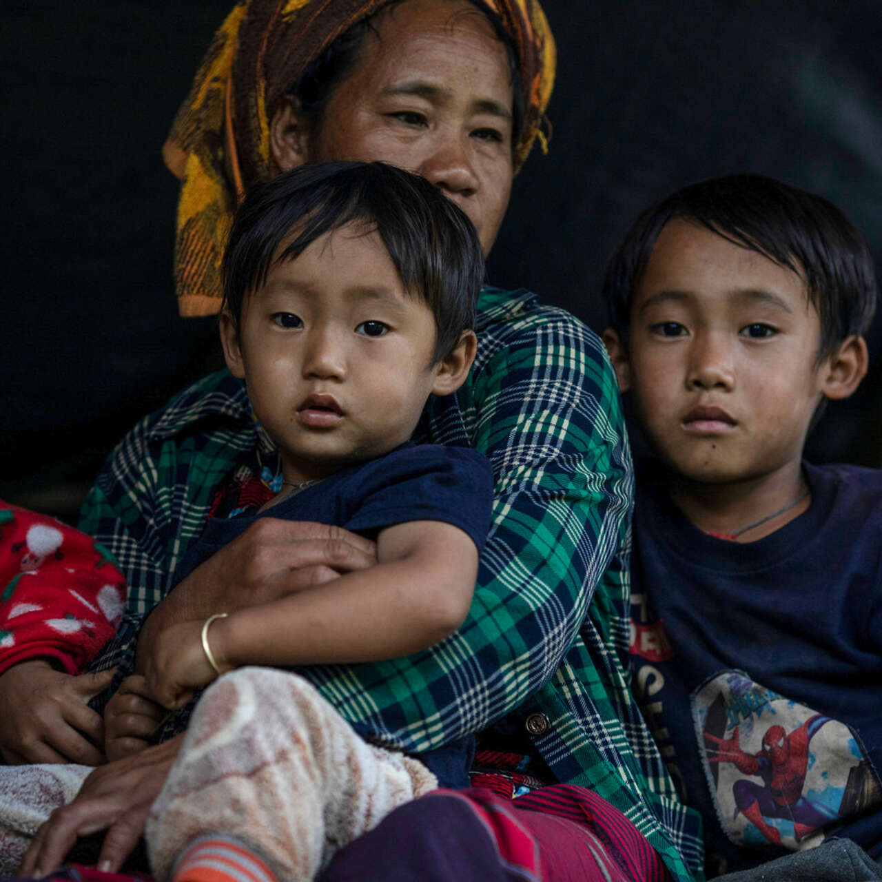 A woman holding a child and surrounded by two children looking into the camera