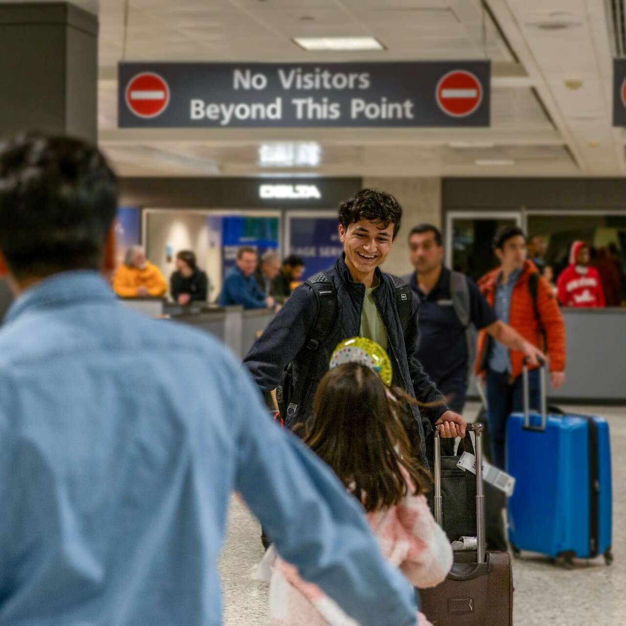 Standing in the airport arrivals, a father smiling at his two children embracing after being apart
