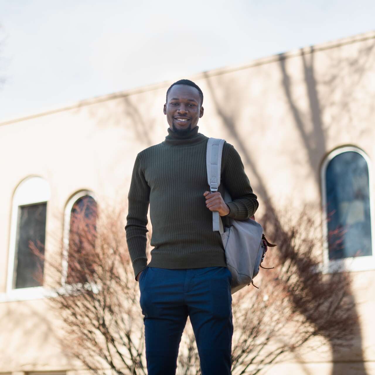 A man stands in front of a building, smiling and posing for a photo.
