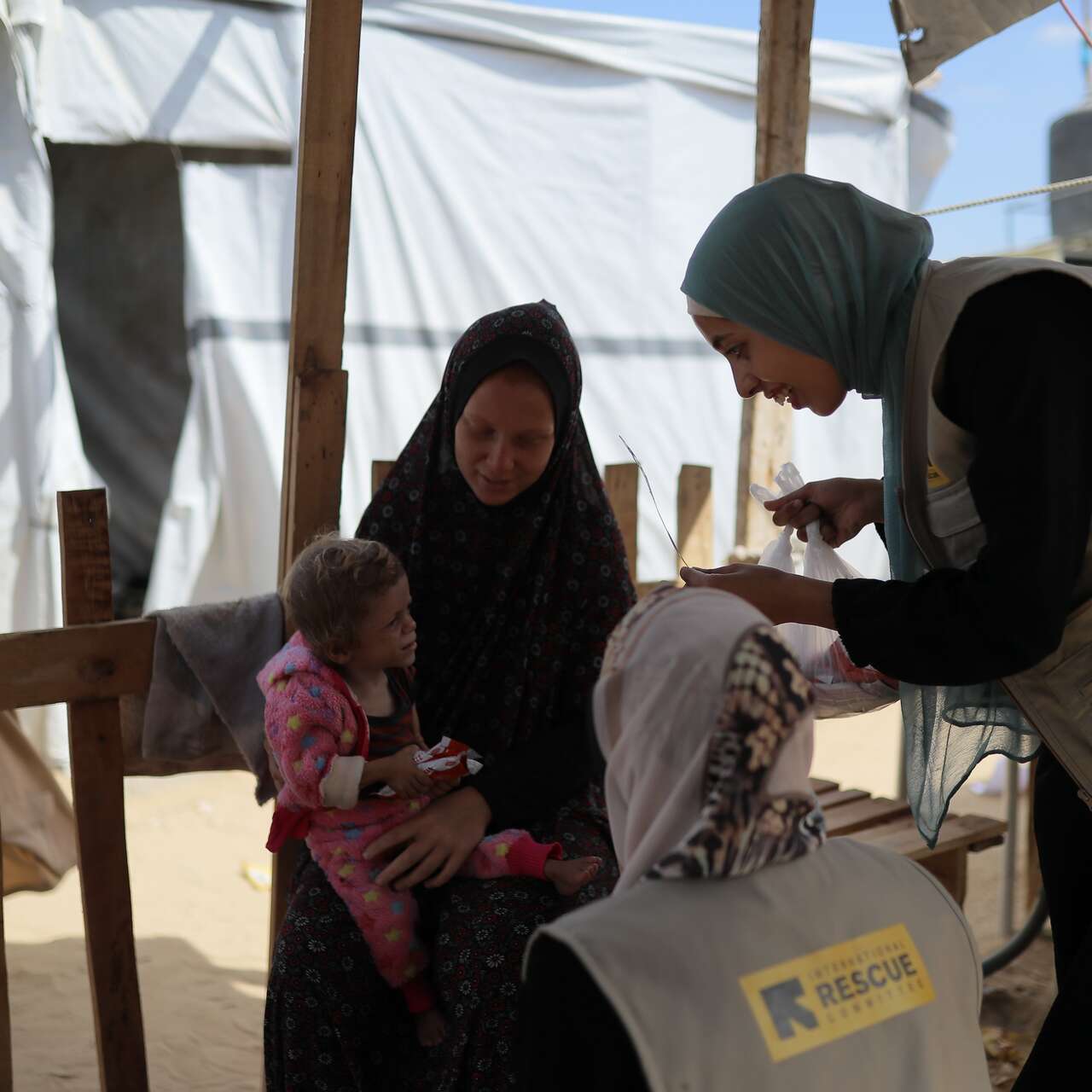 A women with a child on her lap wearing a pink shirt. Another woman is smiling at the child