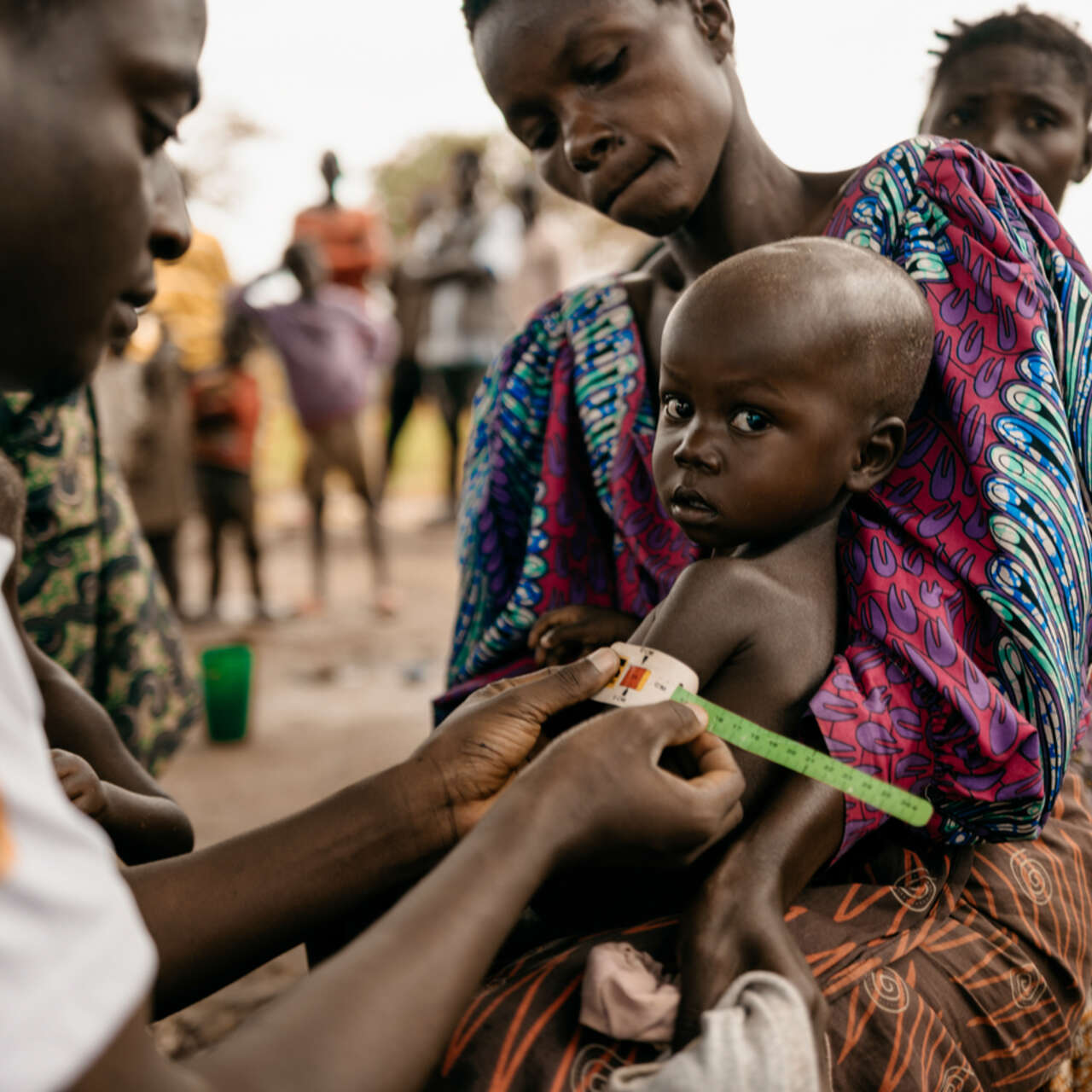En liten pojke sitter i sin mammas knä och får sin överarm mätt av en läkare.