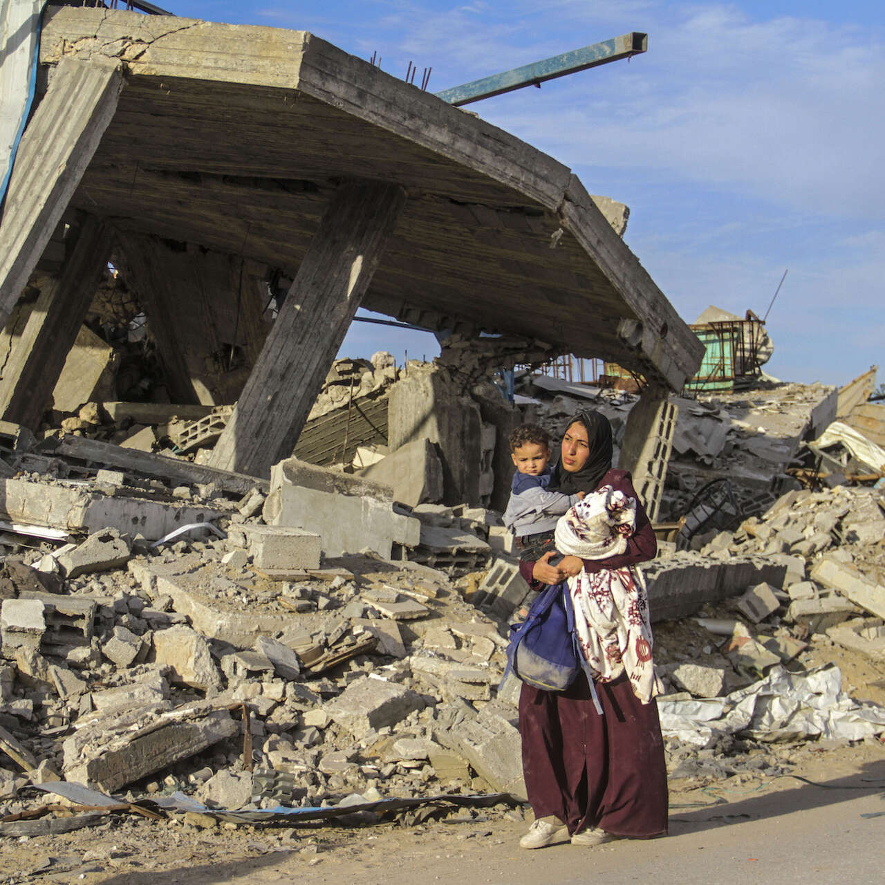폐허가된 가자지구를 한 여성이 아이를 안고 걸어가고 있습니다.