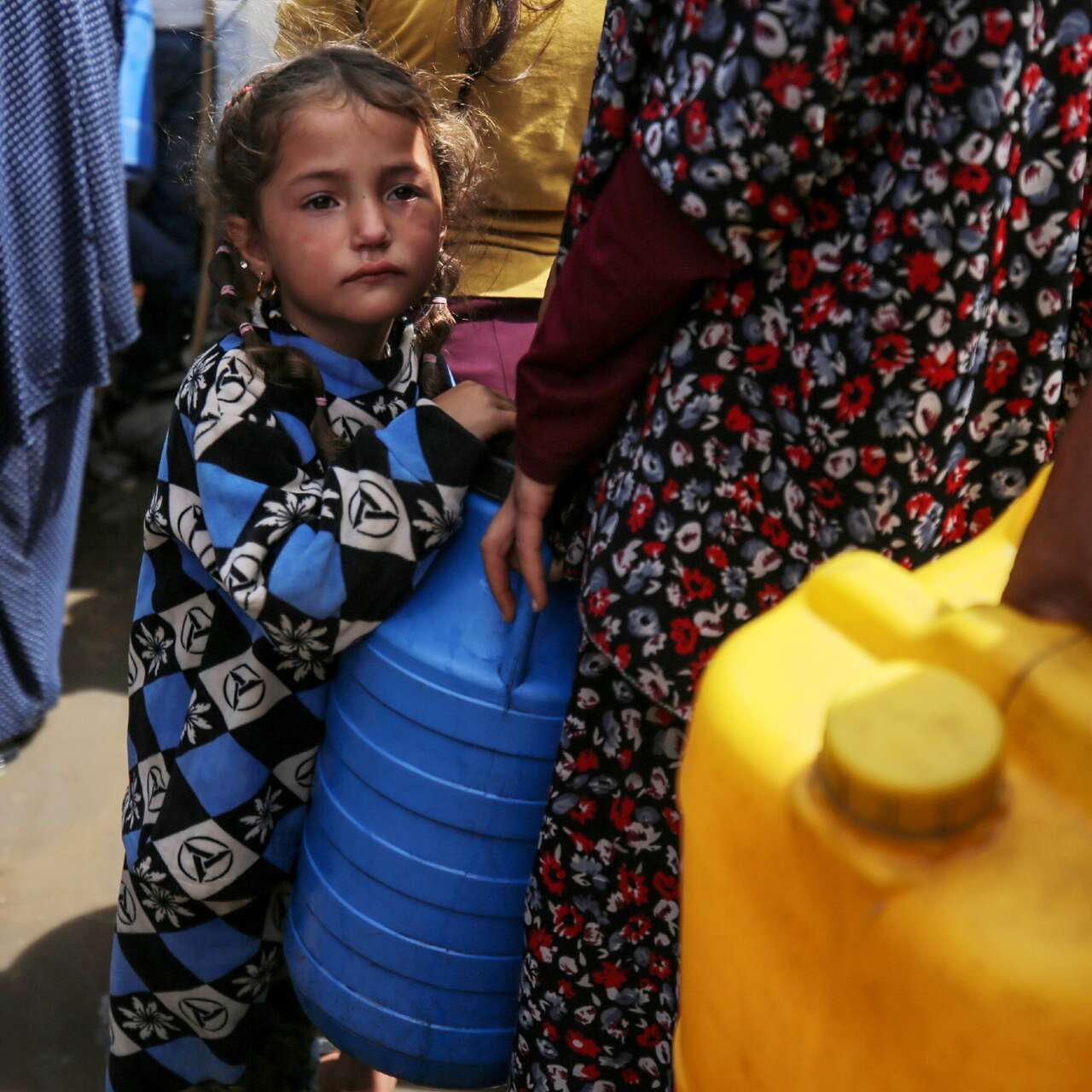 A young girl in Gaza stands by her parent as they collect safe water.