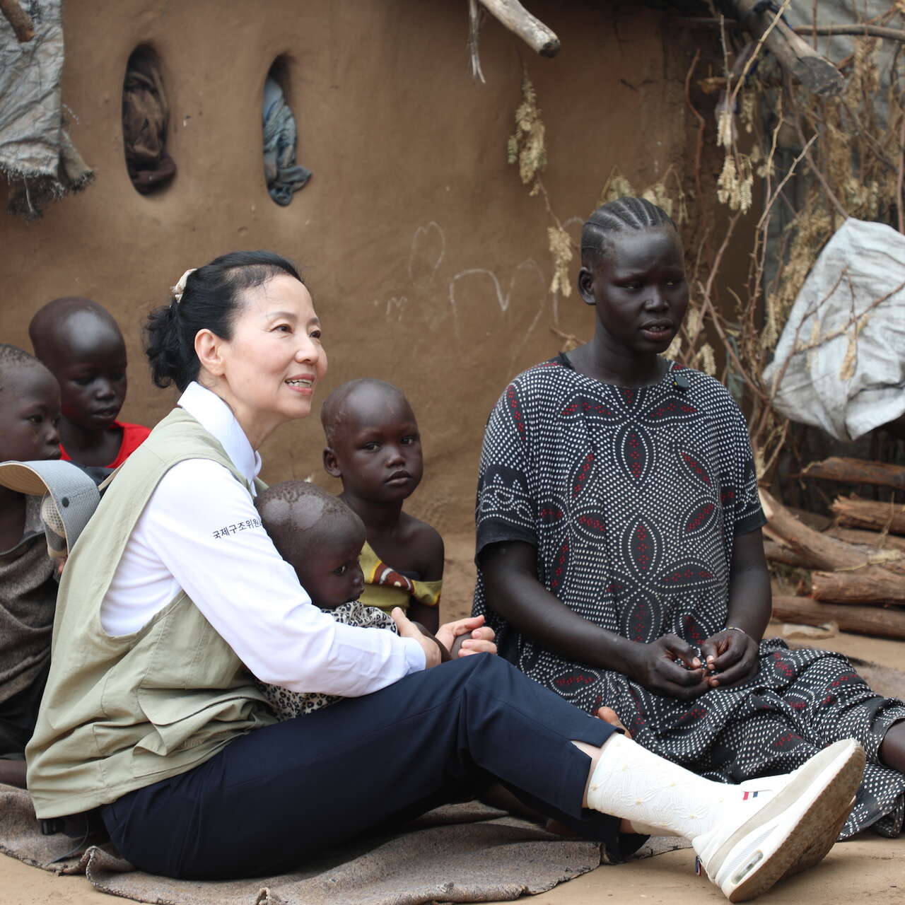 오민애 홍보대사가 한 여성과 아이들과 함께 바닥에 앉아서 이야기를 나누고 있습니다. 