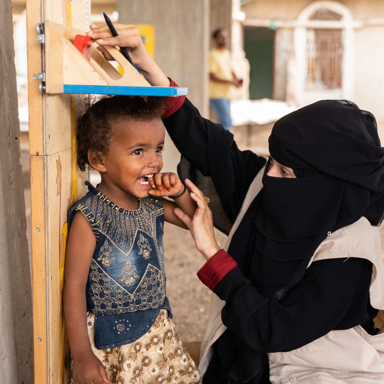 En flicka i ett flyktingläger i Jemen ler när hon blir mätt av personal från RESCUE:s mobila hälsoteam som ger vård på platser som är svåra att nå.