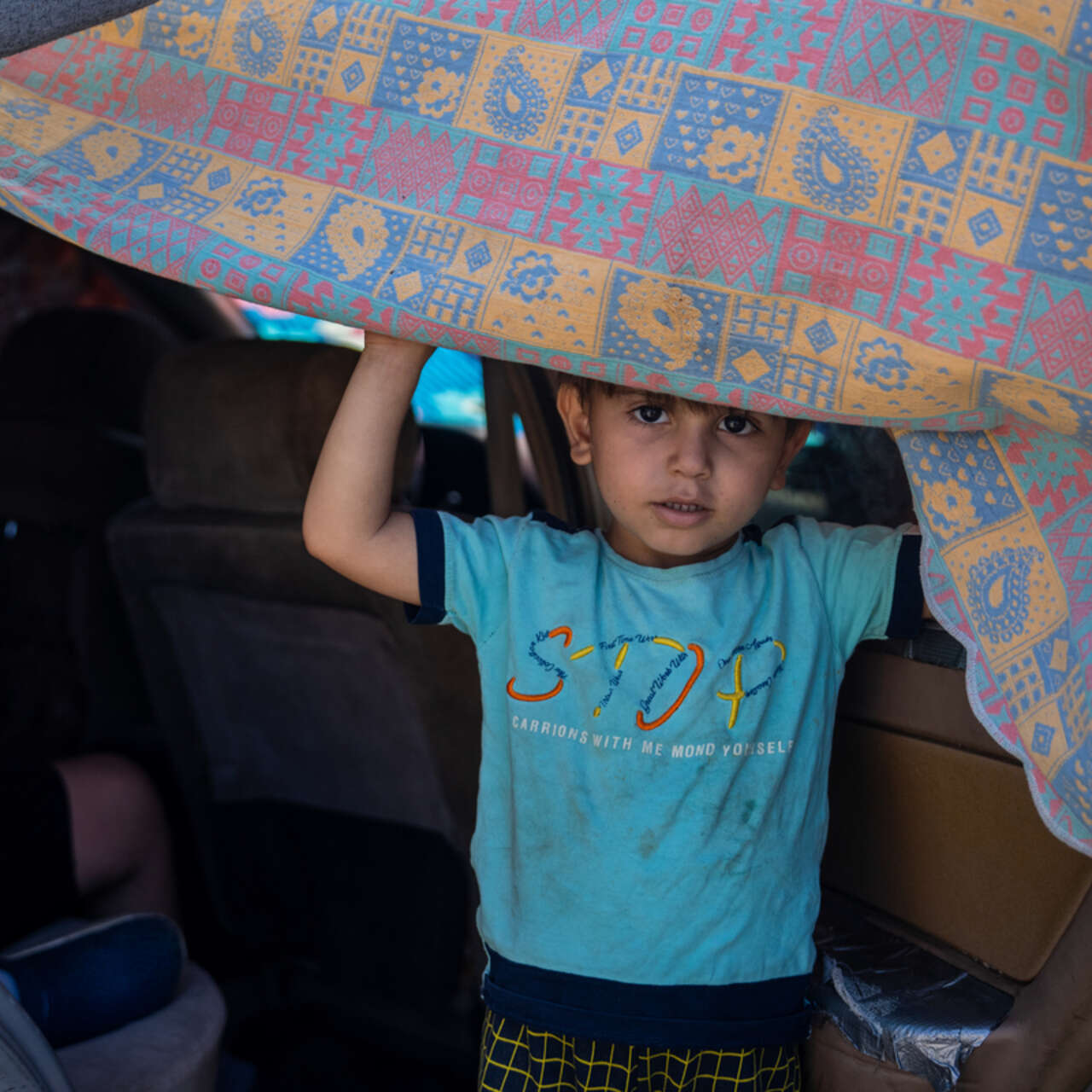 En pojke i Libanon tittar fram under en filt i en bil när hans familj tvingades på flykt under 2024.