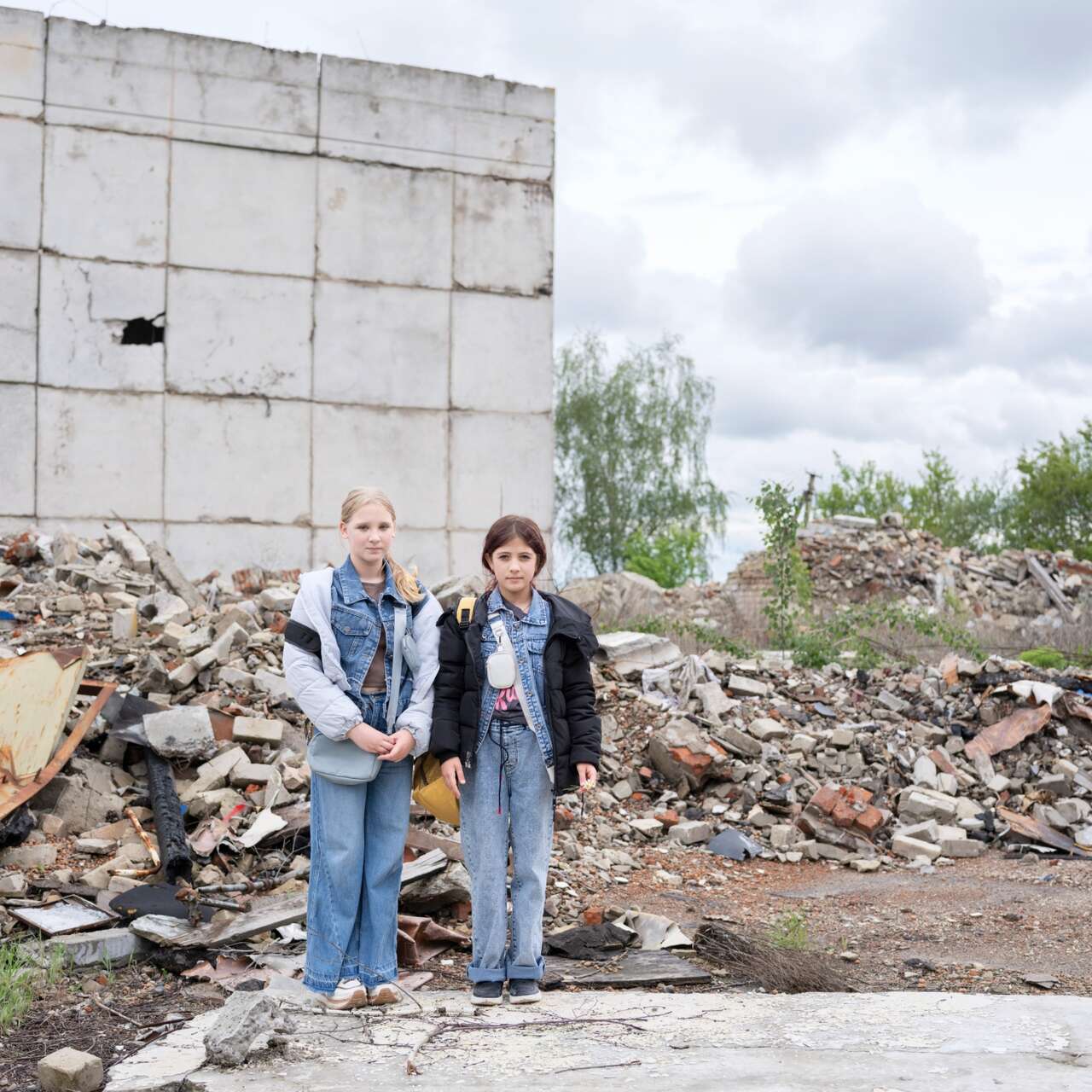 Two Ukrainian children stand in front of bombed structure.