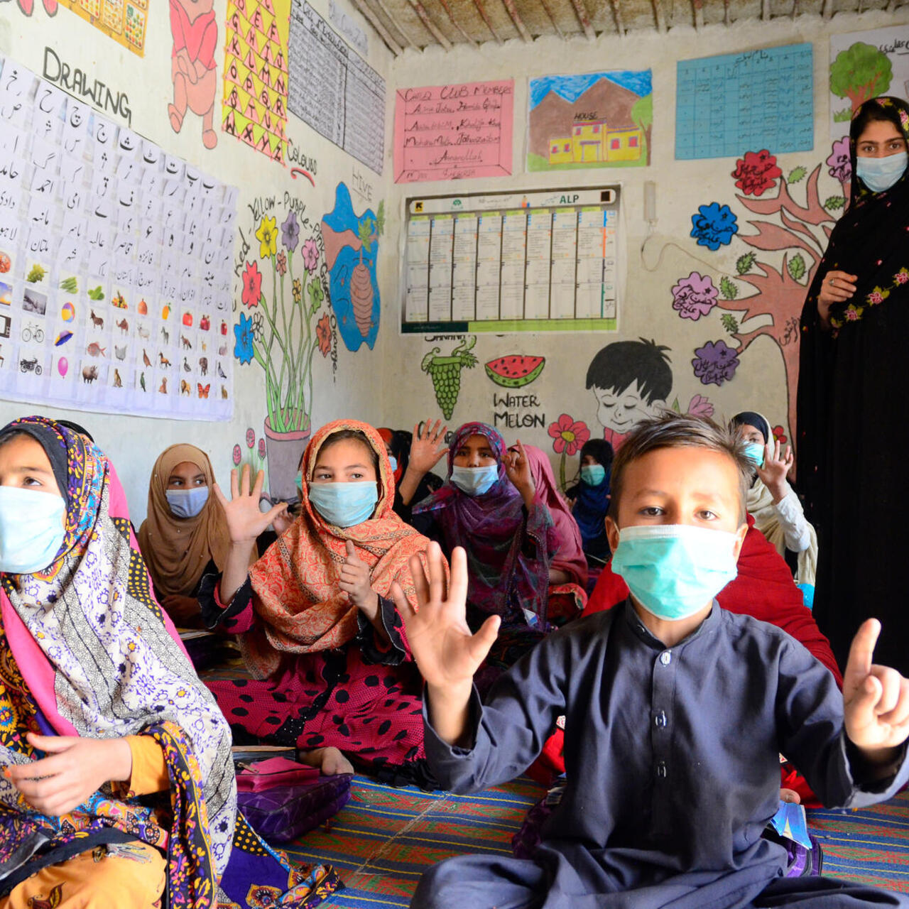 A female teacher in Pakistan with a group of children in a class room all wearing masks