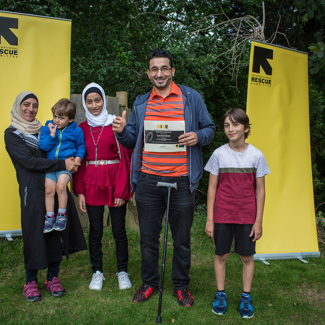 IRC client Khalil holds his RISE certificate and smiles with his wife and children.