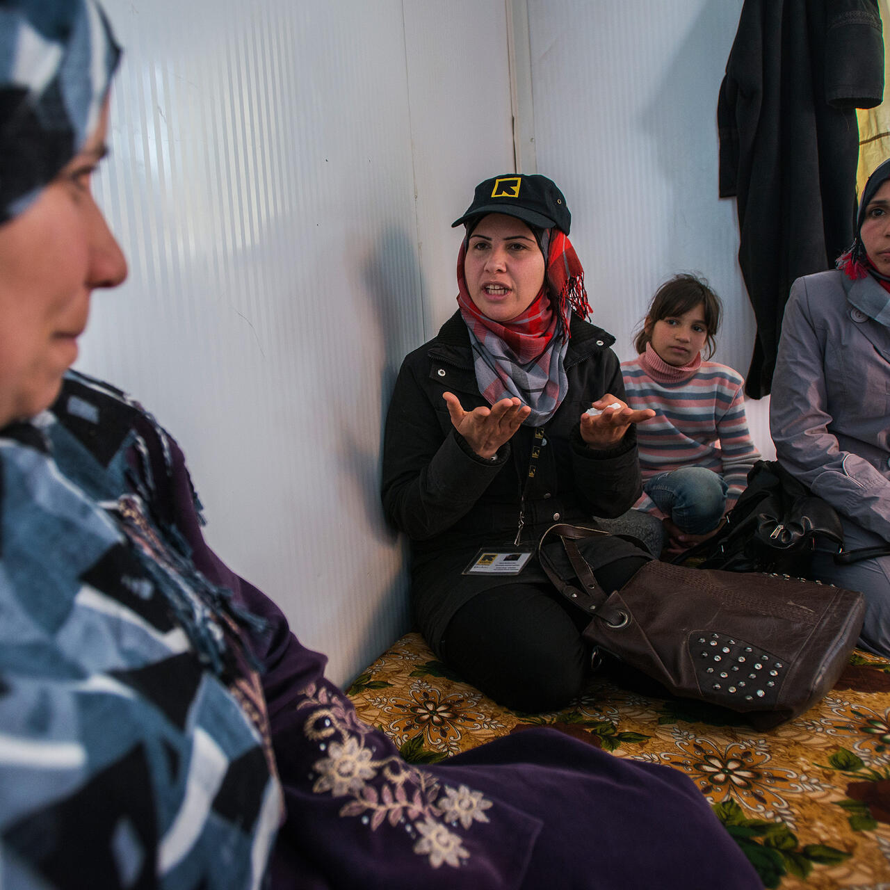An IRC staff member talks with a Syrian refugee family seated on cushions in their shelter in Zaatari refugee camp in Jordan.