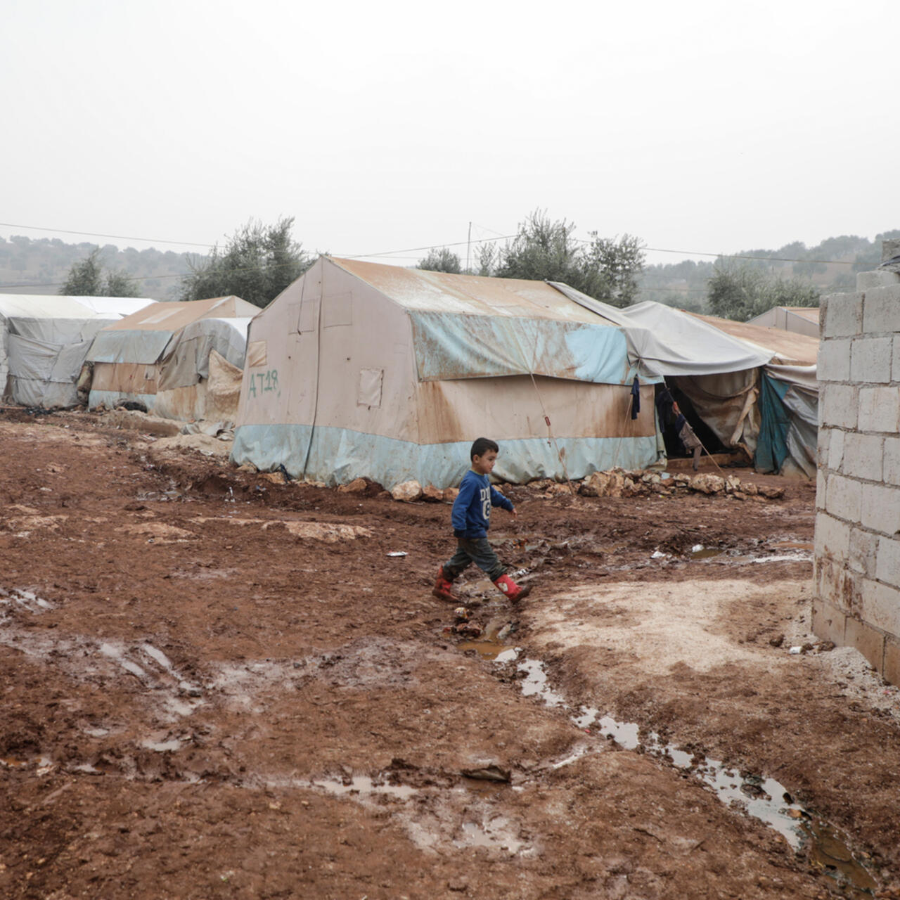 A Syrian boy walks through the mud past tents for displaced families in Idlib, where the IRC provides aid.
