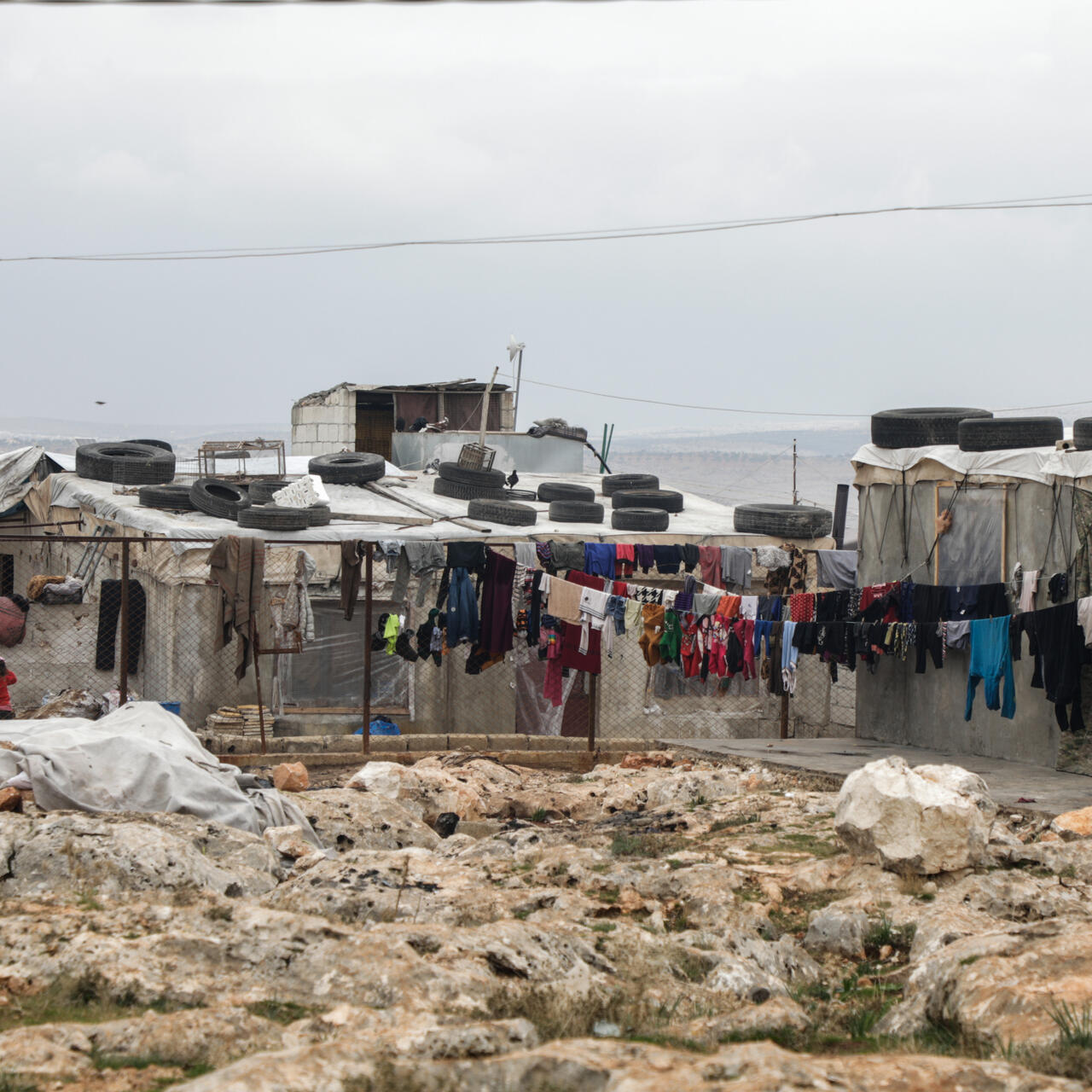 Women and children stand near clothes hanging to dry in a settlement where the IRC is assisting displaced people on the outskirts of the town of Deir Hassan.