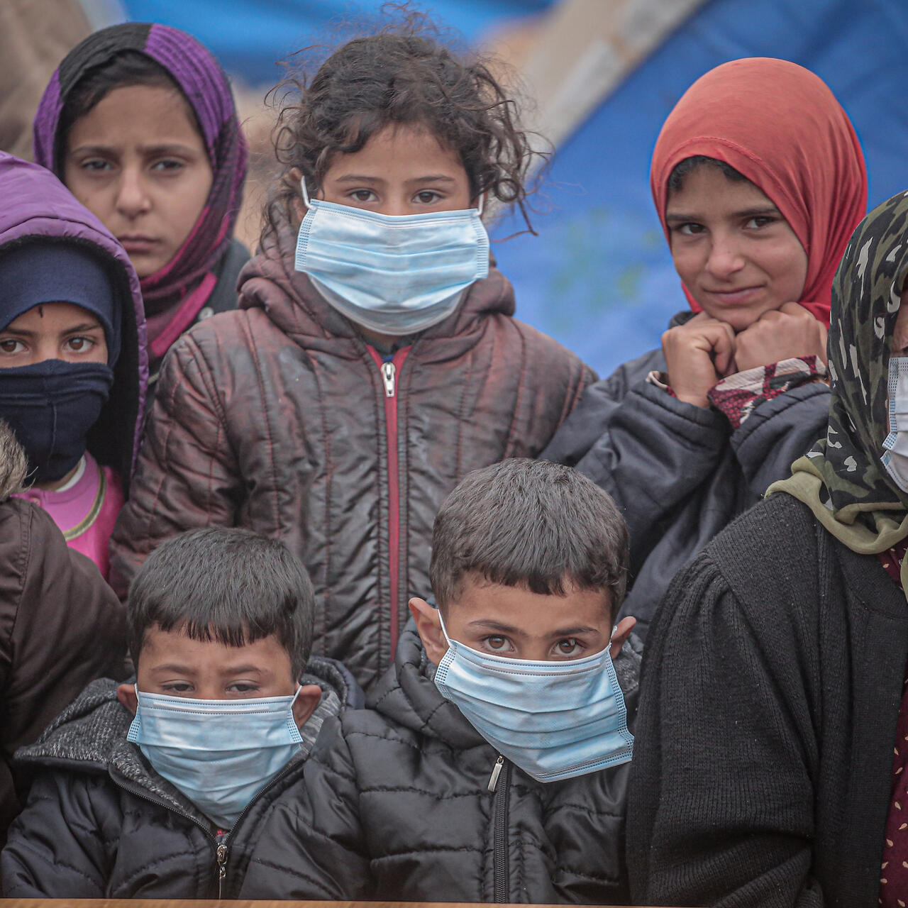 A group of displaced children with an older woman wearing face masks during the COVID-19 pandemic