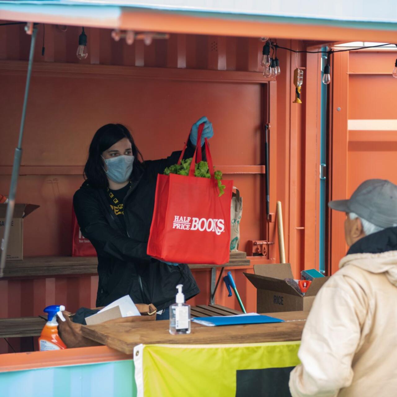 Isabelle Chamberlain, wearing a mask, holds up a red bag full of food that she is about to hand to an IRC client.