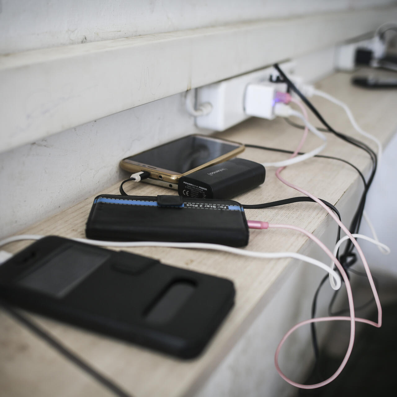 Refugees' ell phones and battery packs charge on a ledge in a refugee camp in Greece