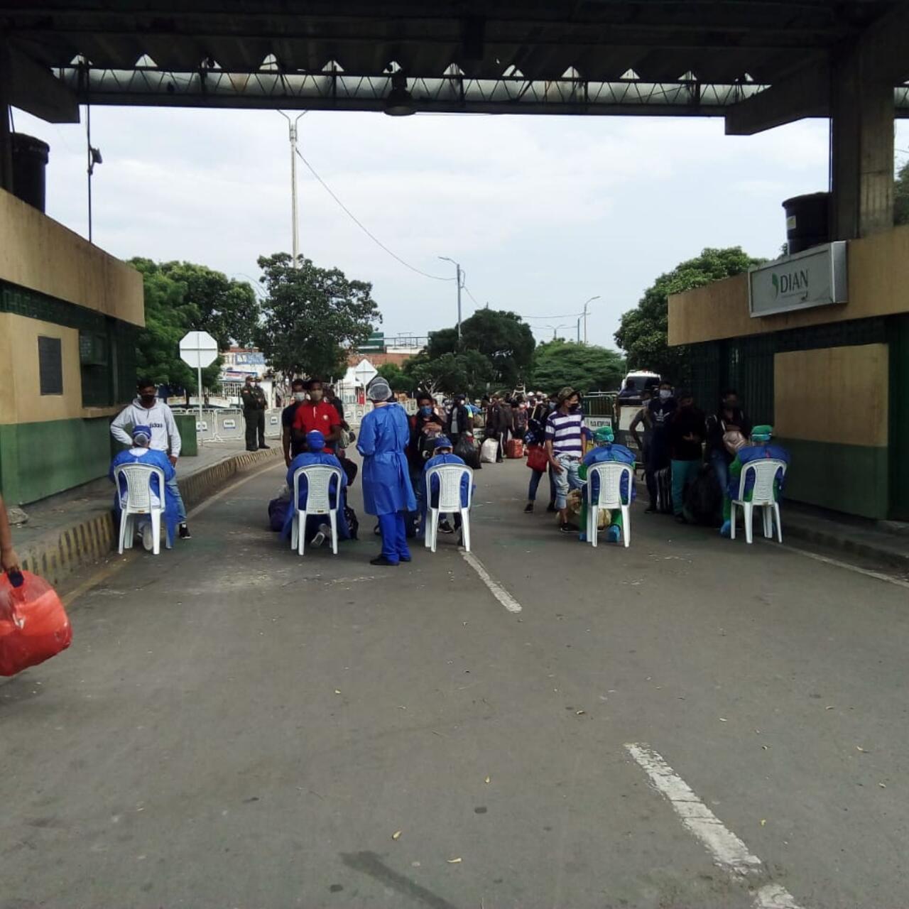 Heath care workers in scrubs sit on chairs or stand offering services to Venezuelans crossing the Simon Bolivar bridge.