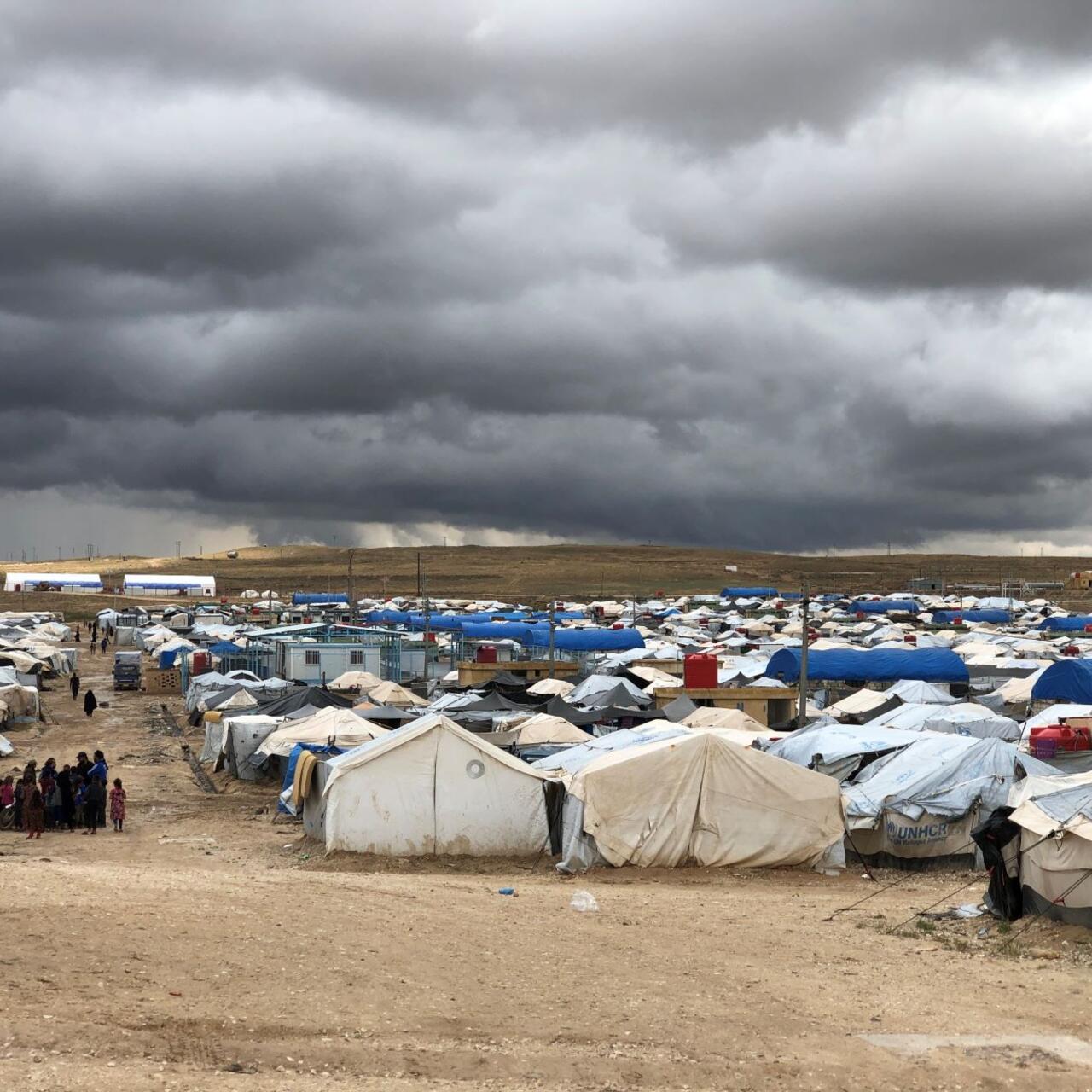 Al Hol camp in northeast Syria. A group of refugees stand next to a cluster of tents. 