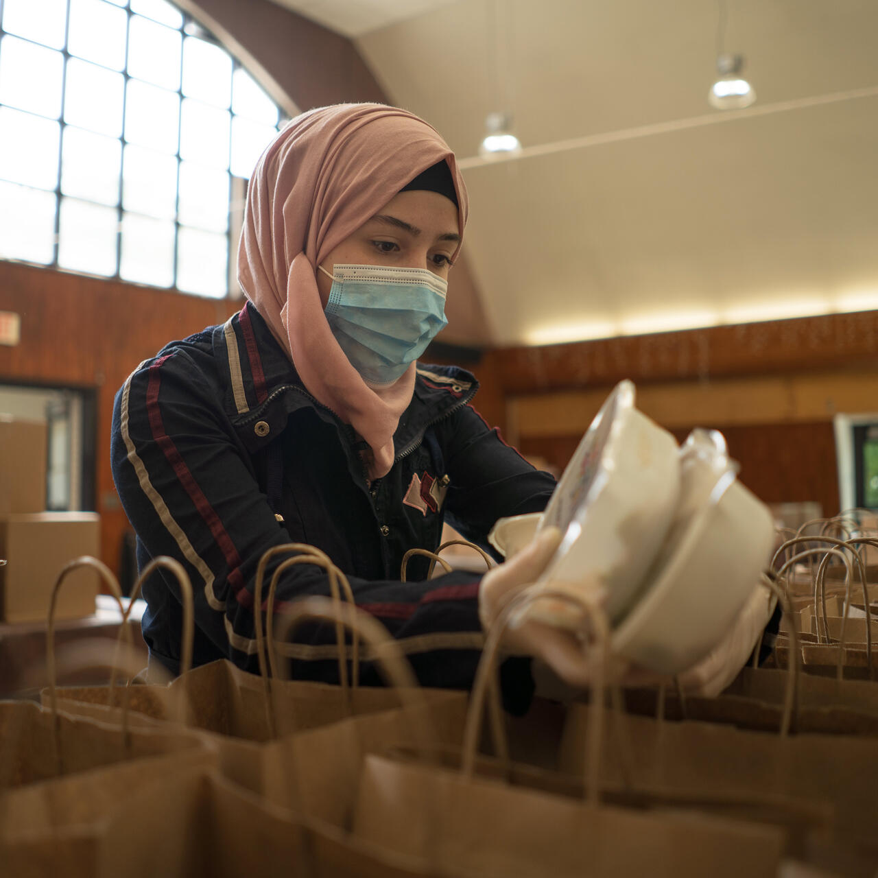 Rania Abou, wearing a mask, puts two containers of food inside paper bags to be given away as part of her work with the IRC and World Central Kitchen.