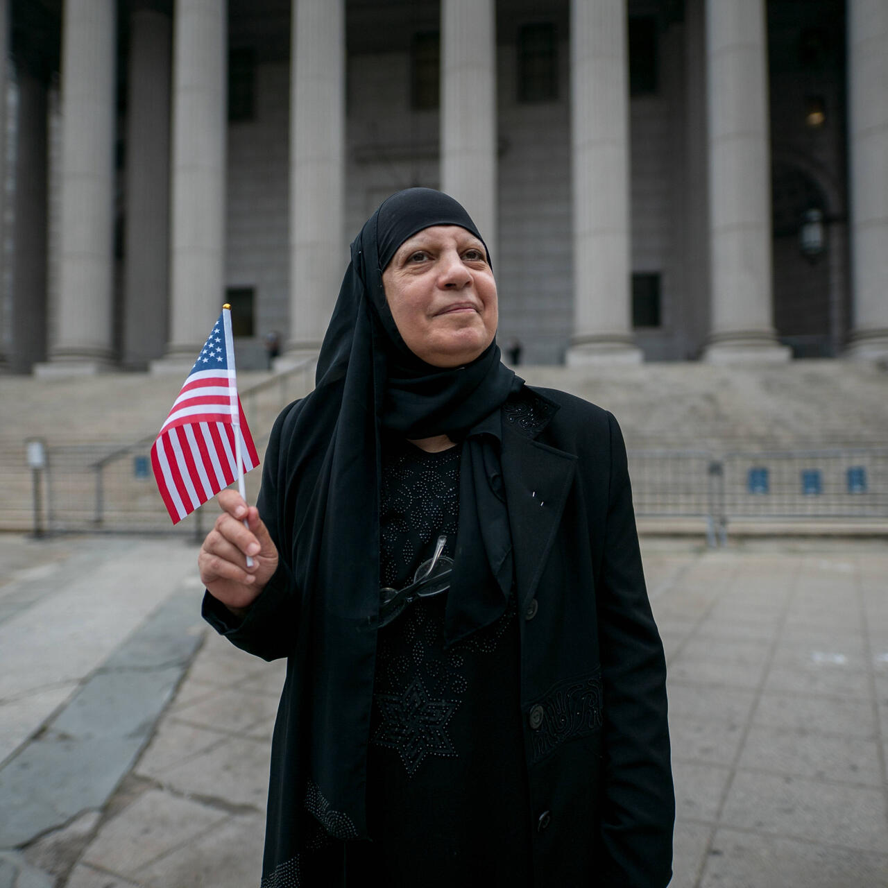 Maha al-Obaidi stands in front of a government building holding an American flag.