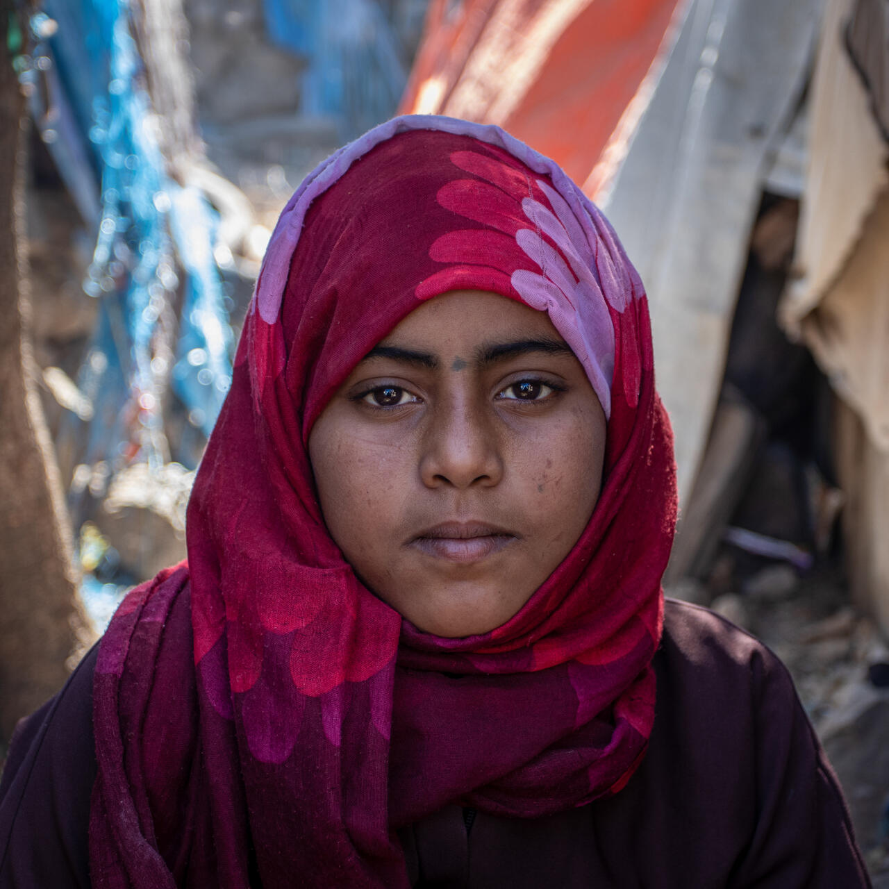 A displaced 11-year-old Yemeni girl named Na'aem stands amid makeshift tents looking directly at the camera with a serious expression.