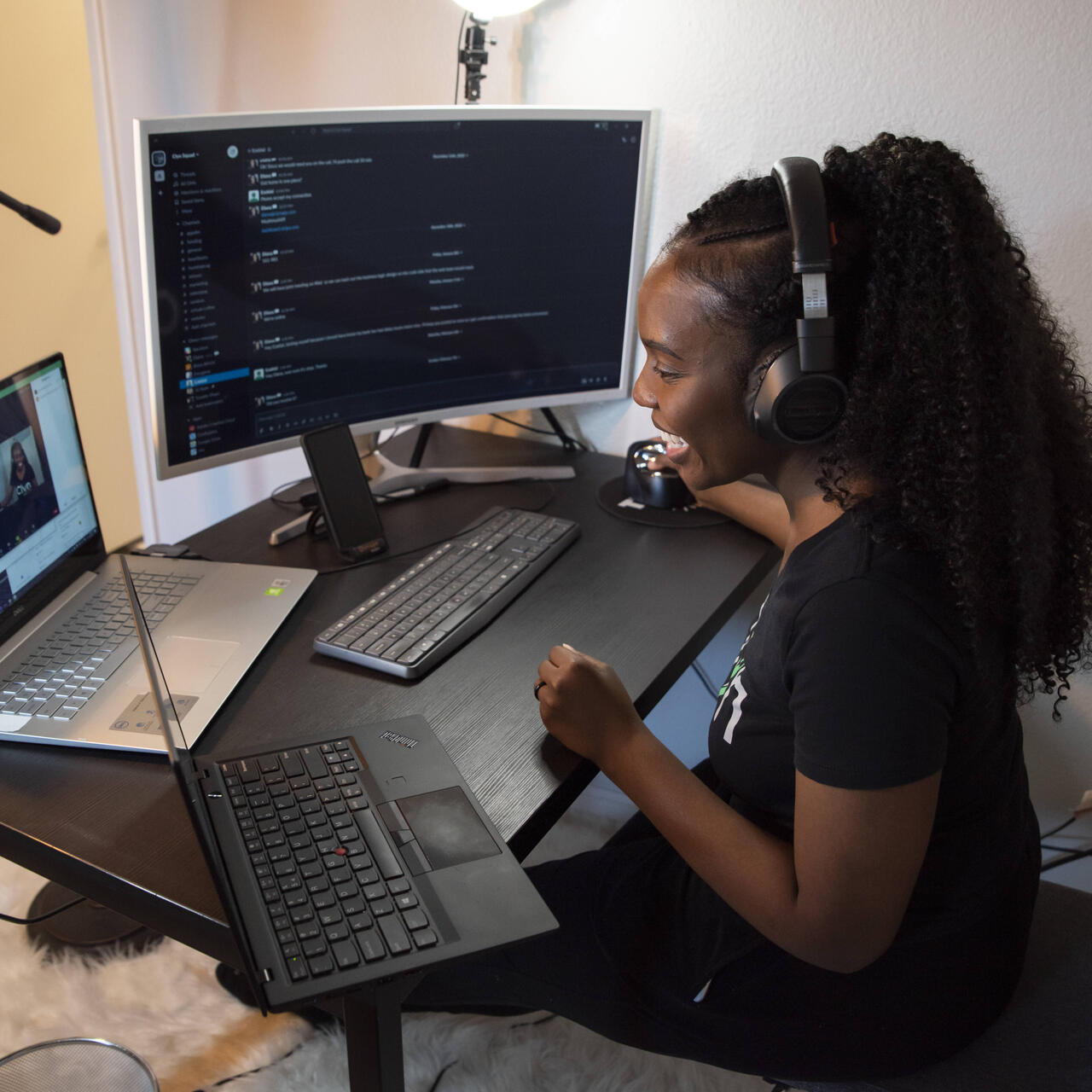 Wearing headphones, Diana Muturia smiles and looks at her computer while working on her app, Clyn.
