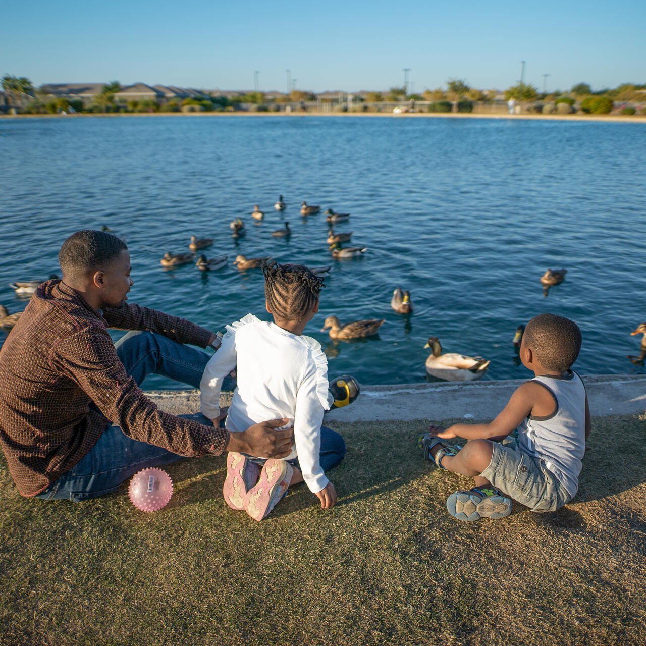 Congolese refugee Robert Sebatware sits with his two young children watching ducks swim in a pond in Phoenix, Arizona