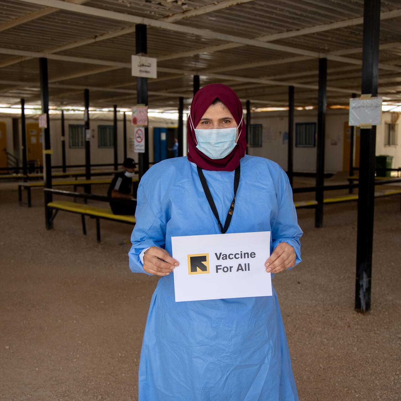 Hend Abu Dabour, an IRC nurse, holds up a sign saying Vaccine For All in the waiting area at the IRC's clinic in Zaatari refugee camp, Jordan