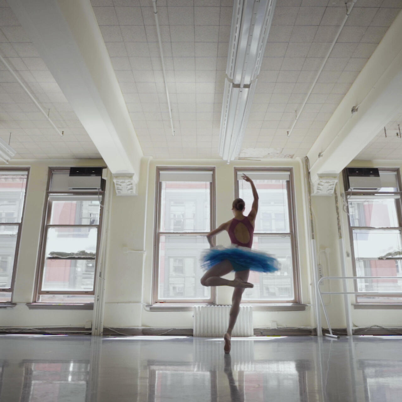 Ballet dancer Christine Shevchenko, wearing a tutu, pirouettes before the windows of a rehearsal studio.