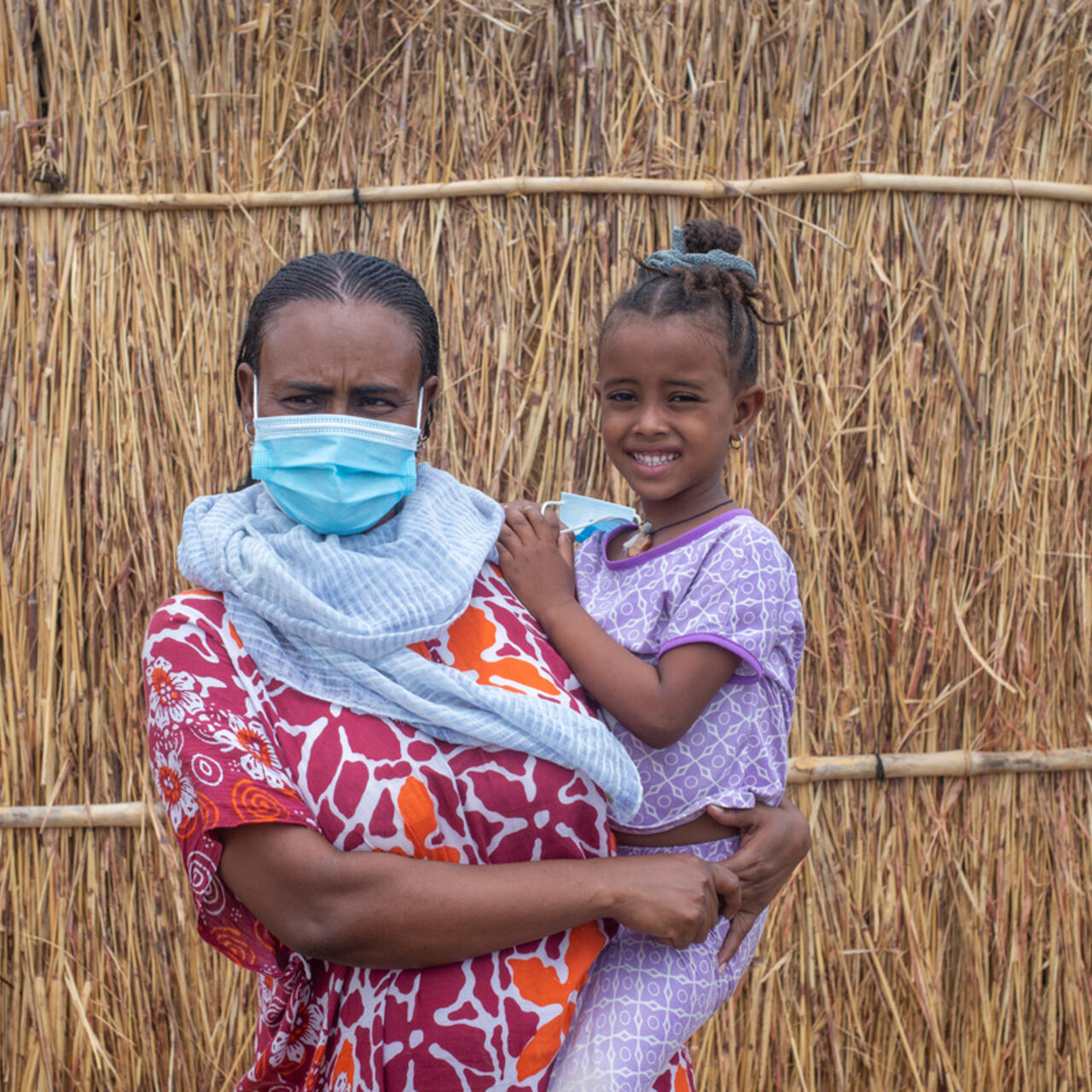 30-year old Azmera from Tigray holds her young daughter outside her thatched shelter in Sudan.