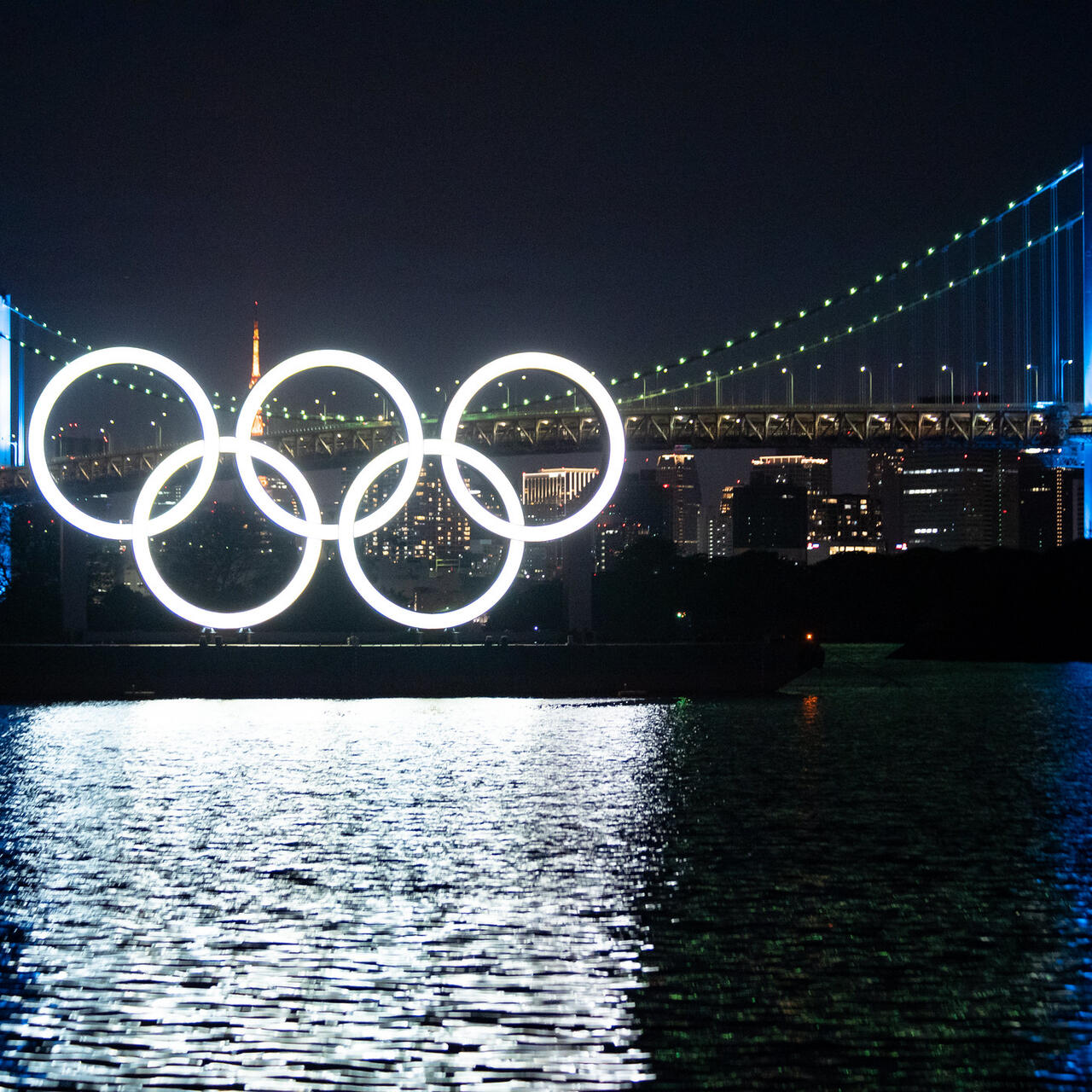 Monument of Olympic Rings at night, set on a barge in Tokyo with a bridge behind it for Tokyo 2020