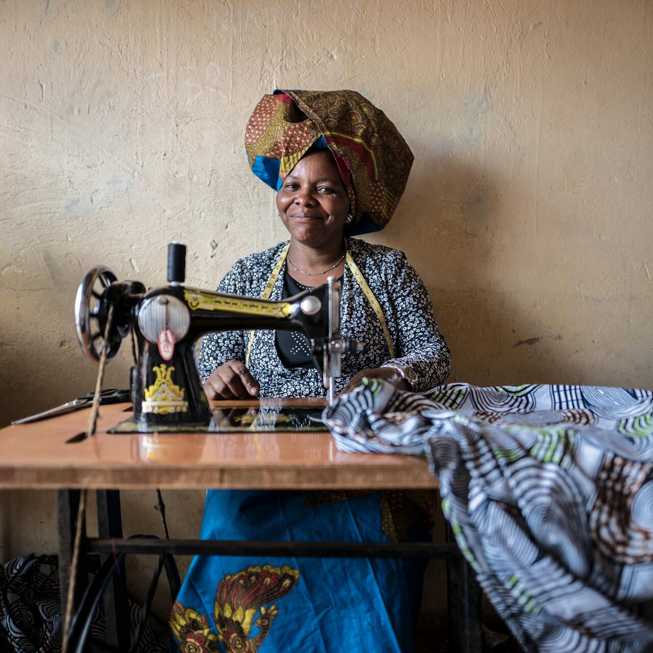 Domitila Kaliya, a Congolese refugee, sits smiling at her sewing machine with fabric in front of her