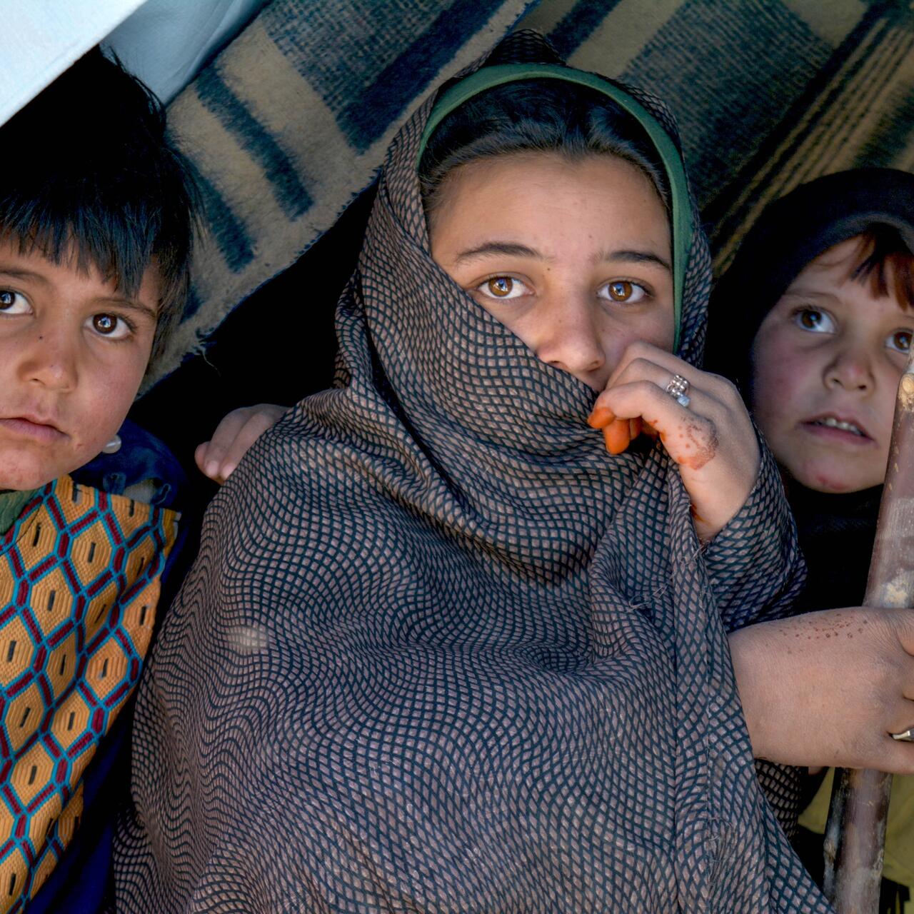 Three Afghan children sit inside a makeshift tent