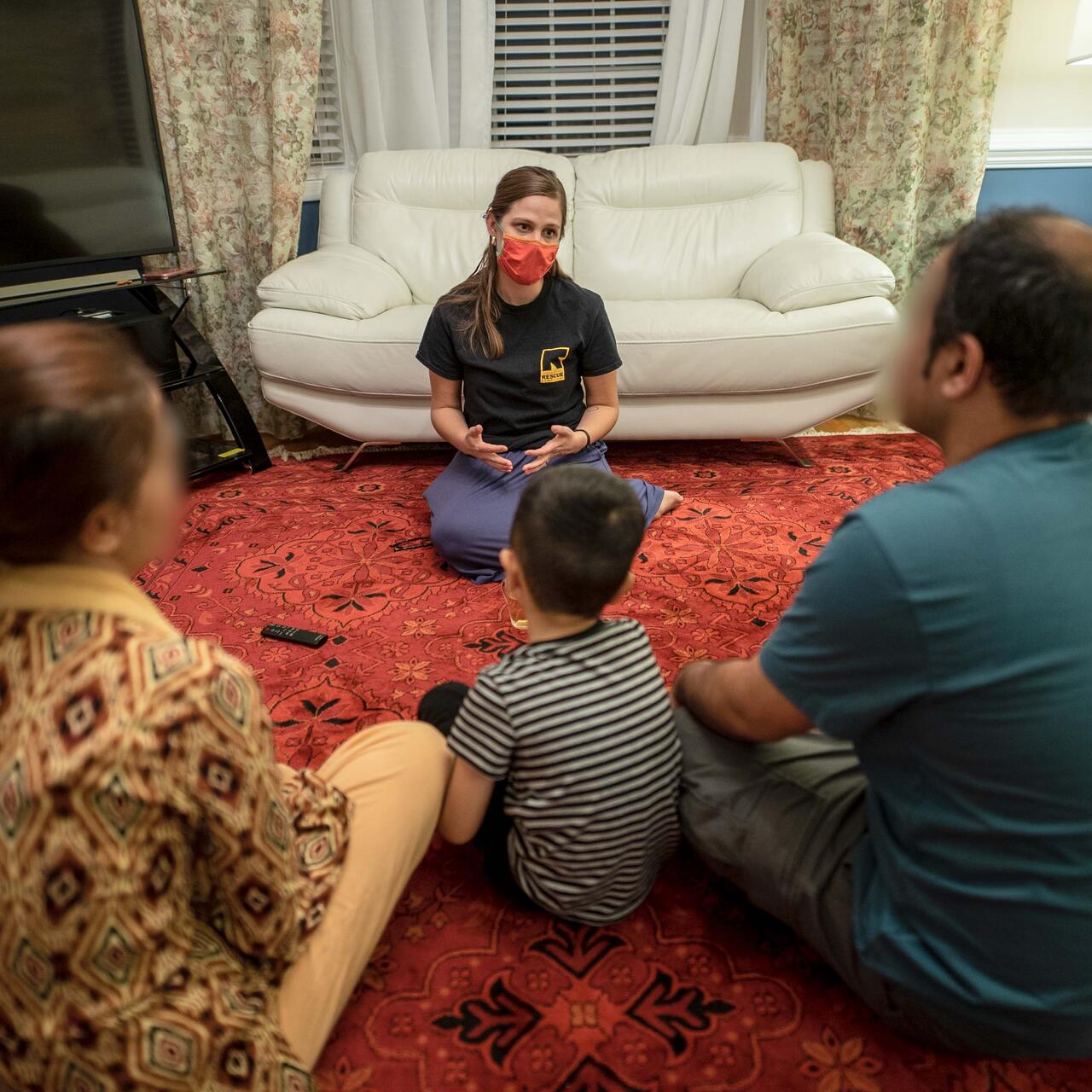 An IRC staff member sits and speaks with an Afghan man, woman, and child.