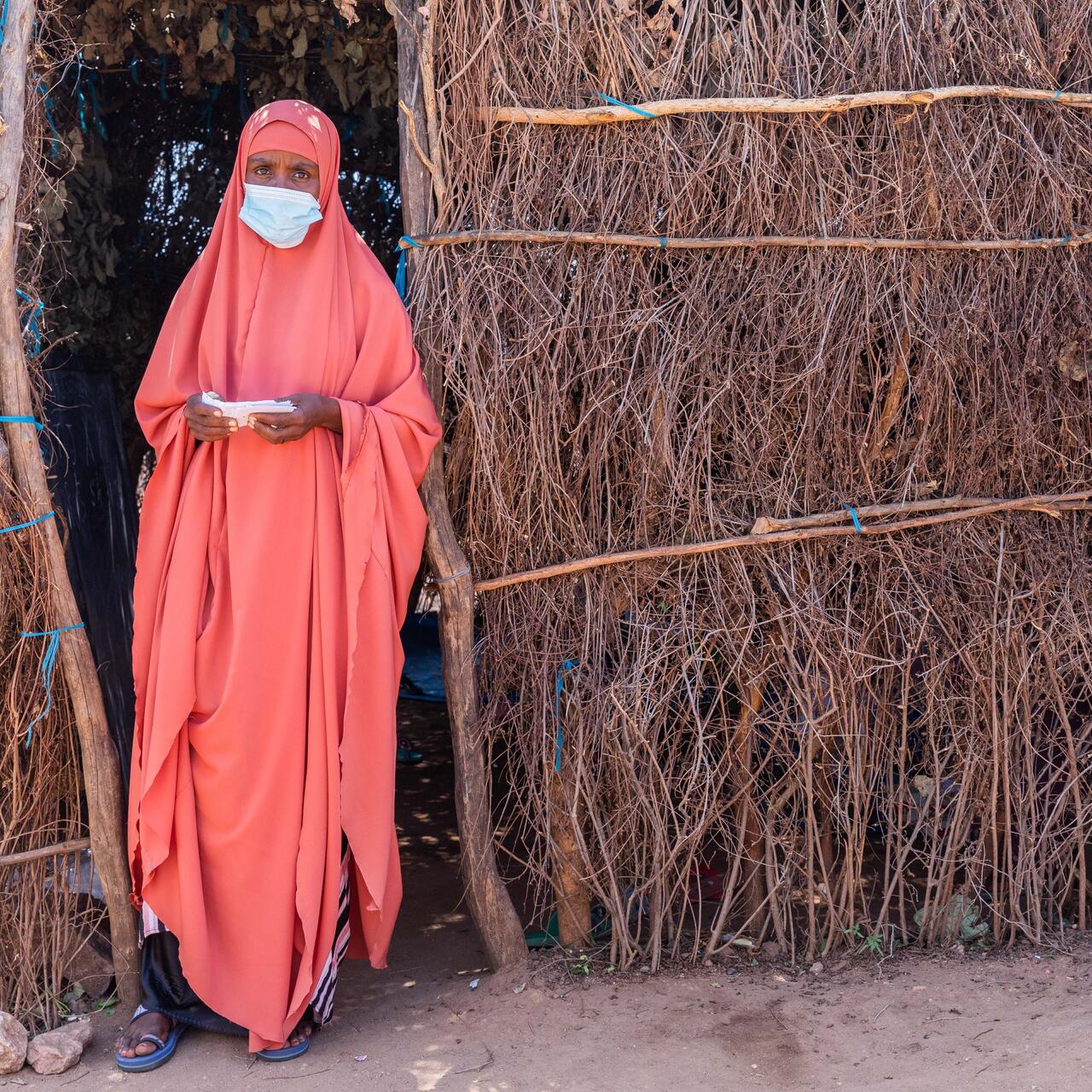 A teacher wearing a mask to protect against the spread of COVID-19 stands outside her makeshift classroom fashioned from branches in a displacmeent camp in Ethiopia.