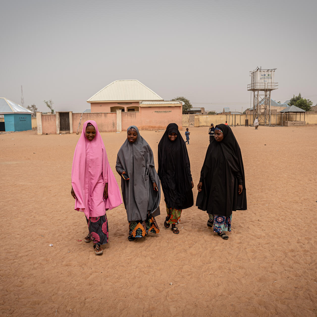 17-year-old Hauwa and four of her friends walk in a straight line across sandy soil near an IRC safe space in Niheria