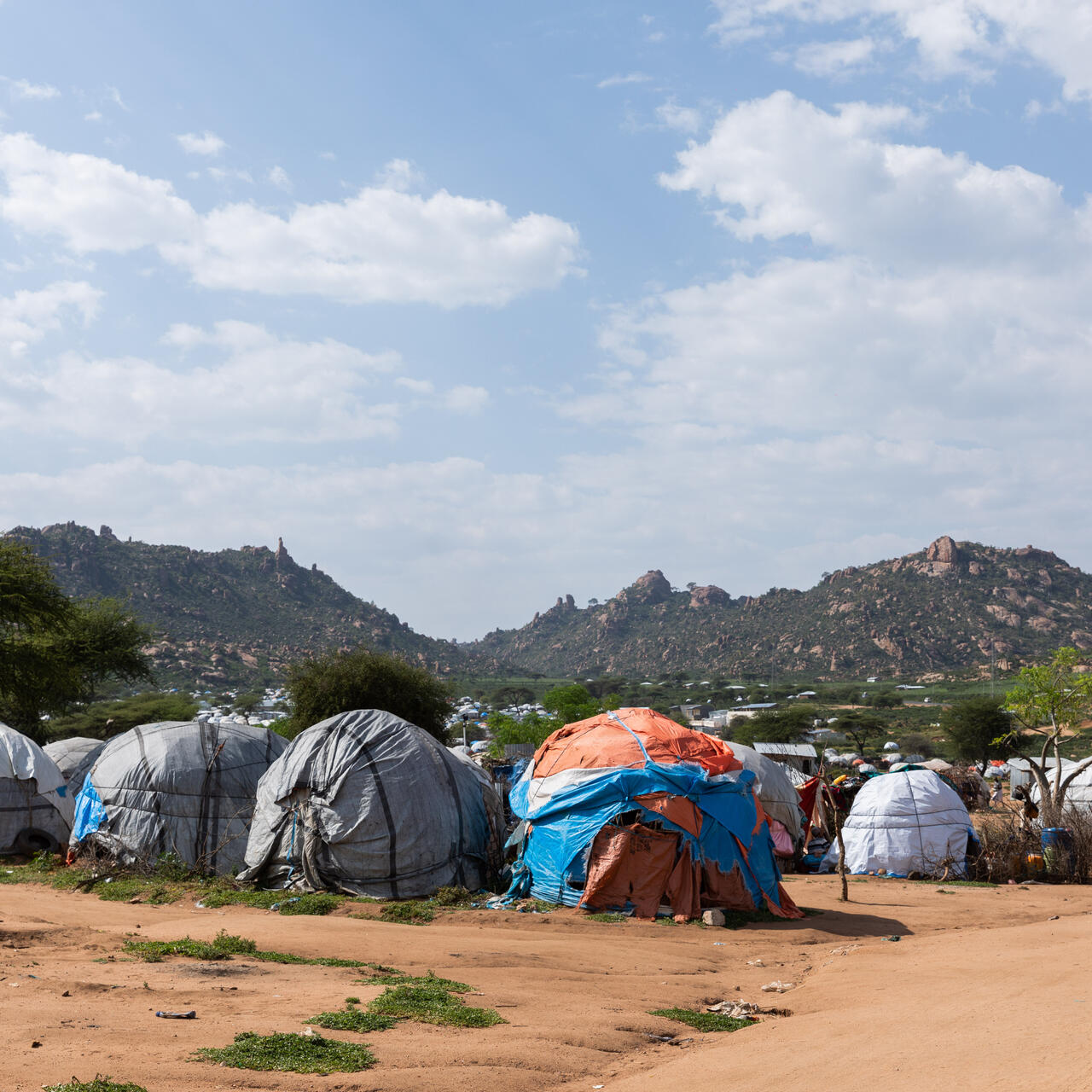 Two children walk on a sandy road past rows of tents where displaced families live in southern Ethiopia against a backdrop of rugged hills.