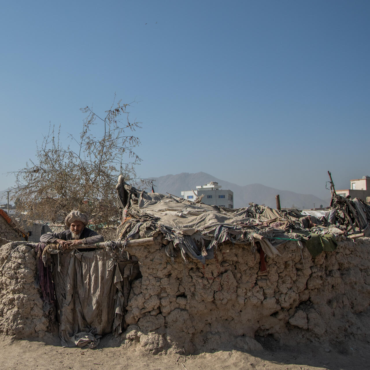 An elderly Afghan man leans on a low wall outside his makeshift home in a camp near Kabul where the IRC is providing emegency cash to displaced families.