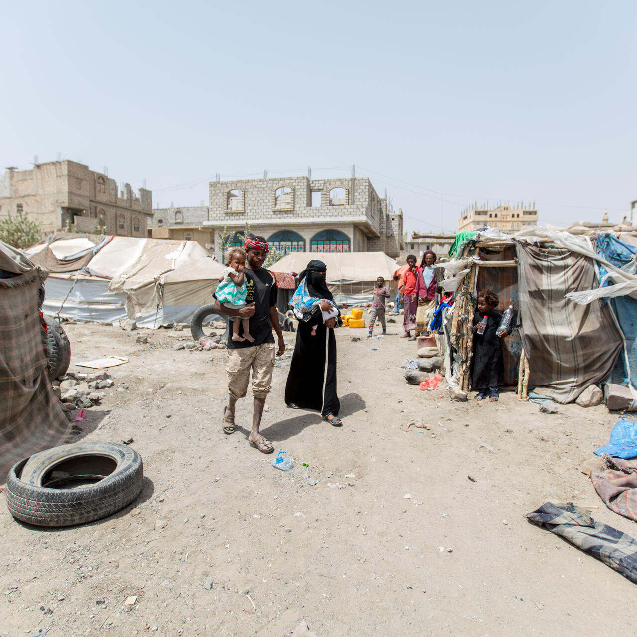 Bodor, carrying her infant daughter walks with her husband and toddler through the camp where they live in a tent alongside other families displaced by the war in Yemen.