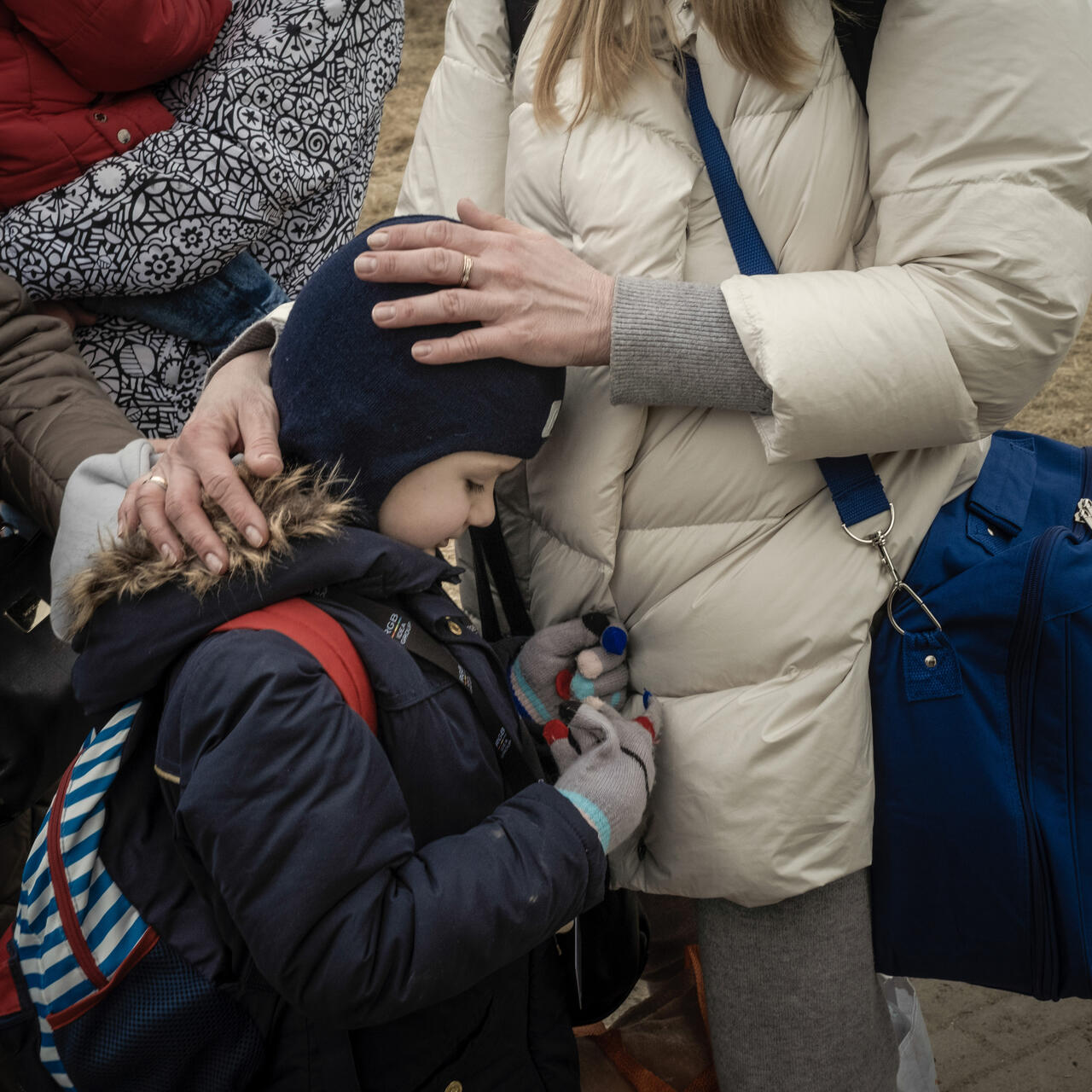 A close up of a child leaning on their mom while she rests her hands on their head.