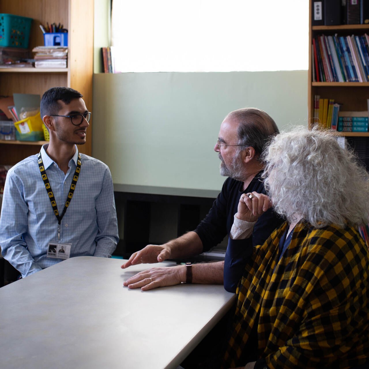 Mandy Patinkin and Kathryn Grody talk with Shir Zad Sarbaz while sitting at a table in the IRC New Jersey office