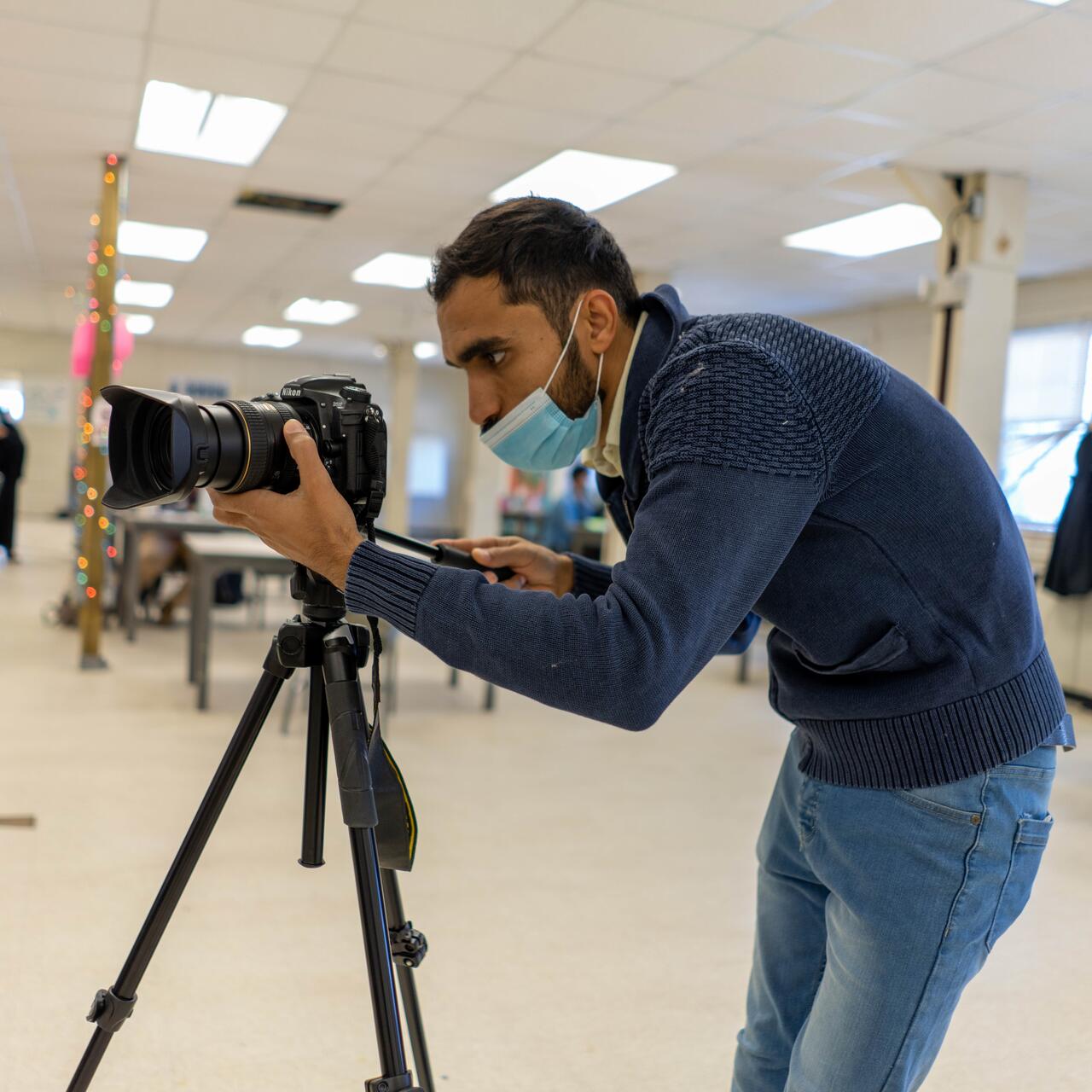Photojournalist Mohammad Anwar Danishyar adjusts the lense of his camera while filming Afghan refugees and the IRCs work in a U.S. government safe haven